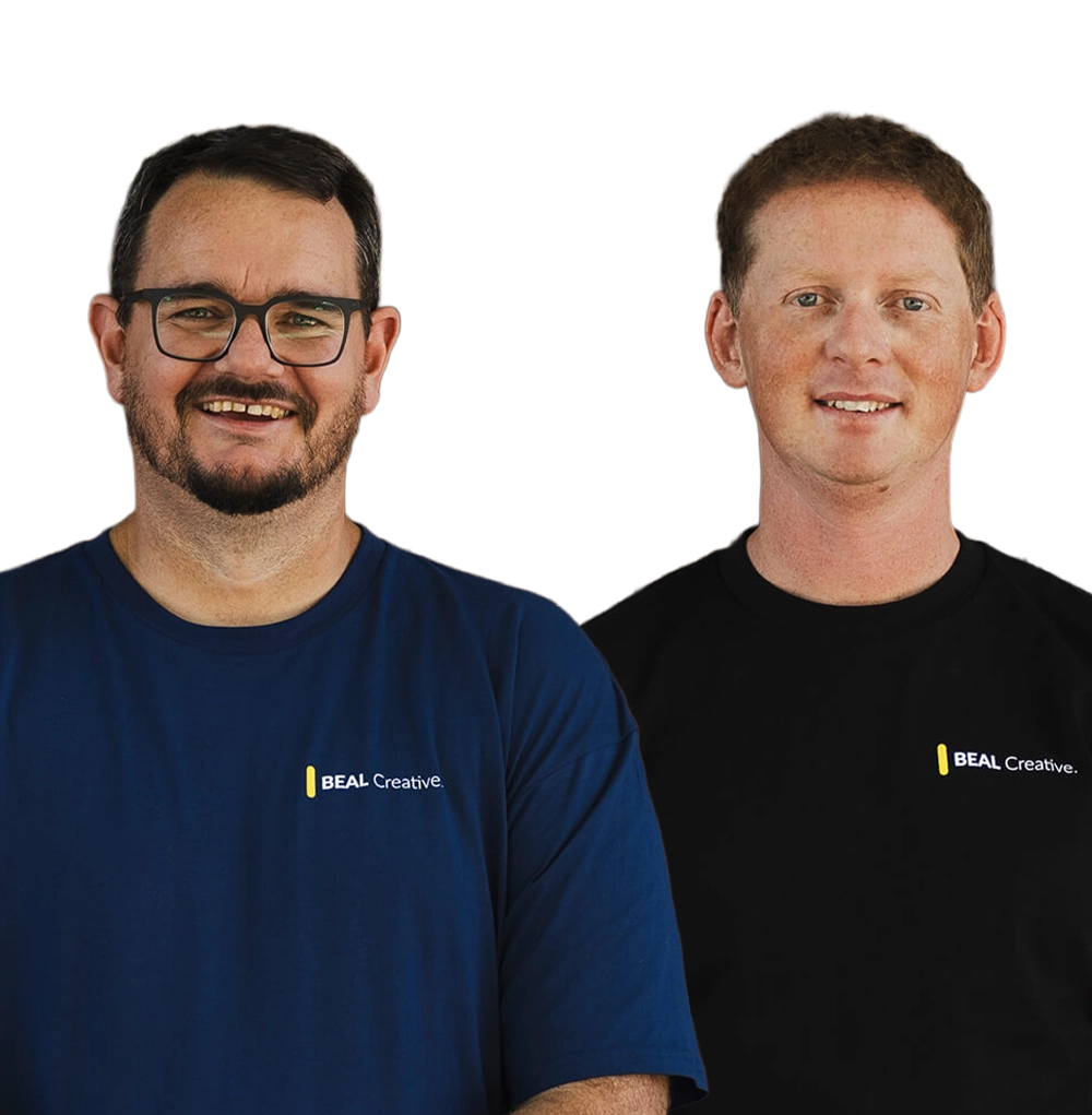 Two BEAL Creative team members wearing branded shirts, smiling at camera against black background.